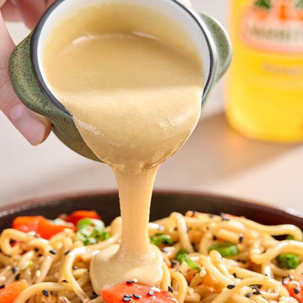 A person pouring Lee Kum Kee Pure Sesame Paste over a bowl of noodles.