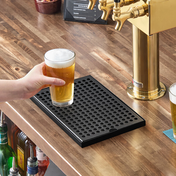 A rectangular black matte surface-mount beer drip tray on a wooden bar counter.