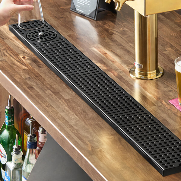 A long, black matte stainless steel beer drip tray with a built-in glass rinser, designed for mounting on a bar surface.