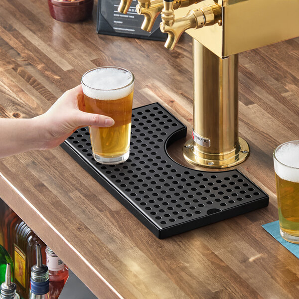A black matte surface-mount beer drip tray with a column cutout placed on a wooden bar counter beneath beer taps.