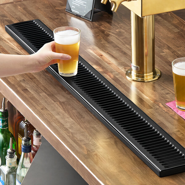 A long, black matte stainless steel surface-mount beer drip tray on a wooden bar counter.