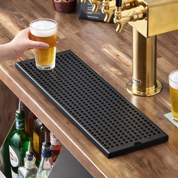 A rectangular black matte surface-mount beer drip tray with a perforated design, placed on a bar counter.