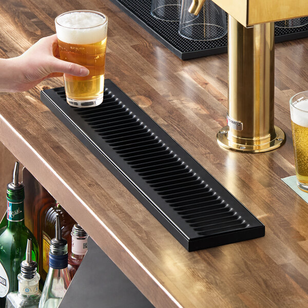 A black matte stainless steel surface-mount beer drip tray measuring 24 by 5 inches on a bar counter.