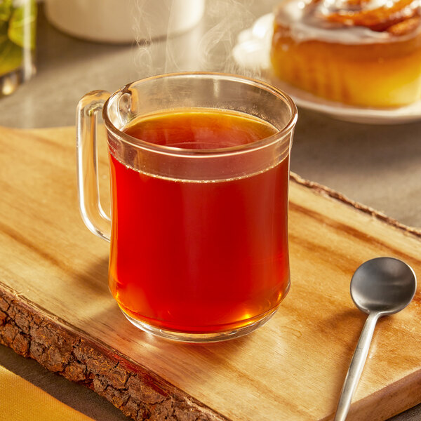 A glass mug of brown Cinnabon coffee on a wooden board with a spoon.