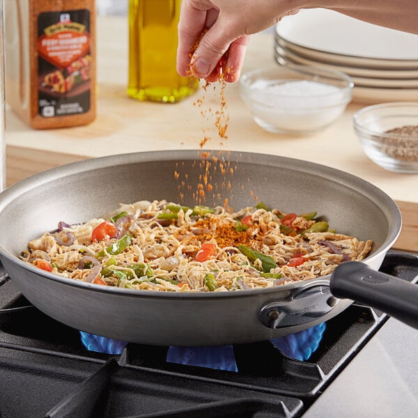 A person pouring McCormick Fiery Habanero and Roasted Garlic seasoning into a pan of food.