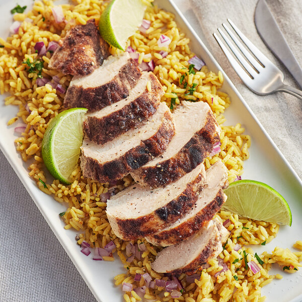 A plate of grilled chicken with rice and lime wedges.