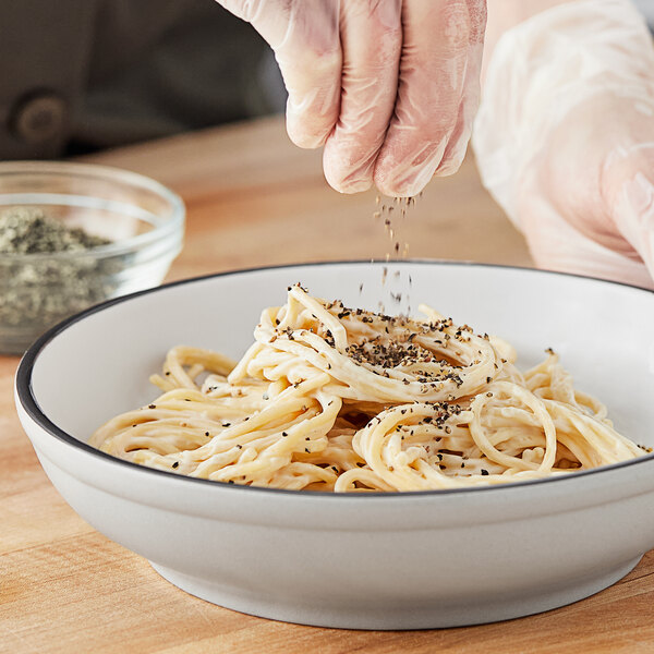 A person sprinkling McCormick Culinary Coarse Ground Black Pepper on a bowl of spaghetti.