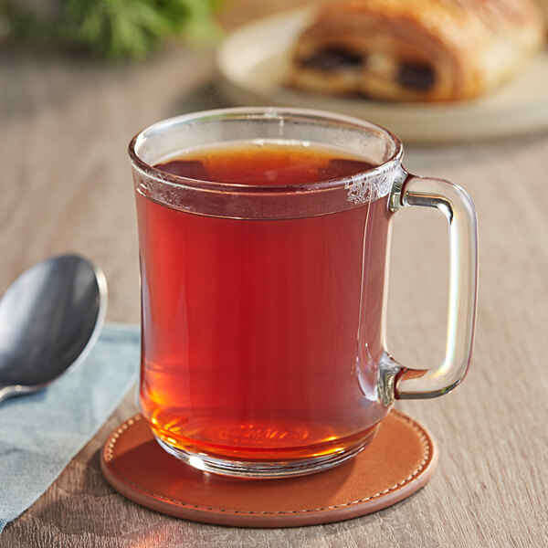 A glass mug of brown Lipton iced tea on a coaster with a spoon.