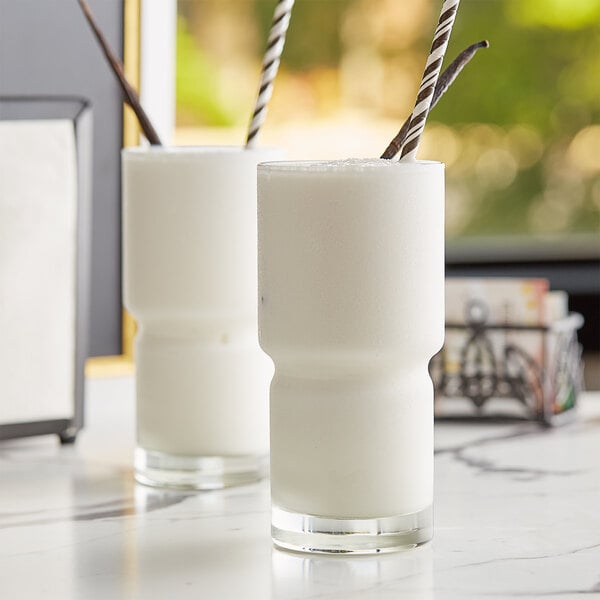 Two glasses of Big Train reduced sugar vanilla smoothies with straws on a counter.