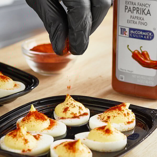 A gloved hand pouring McCormick Extra Fancy Paprika on deviled eggs.