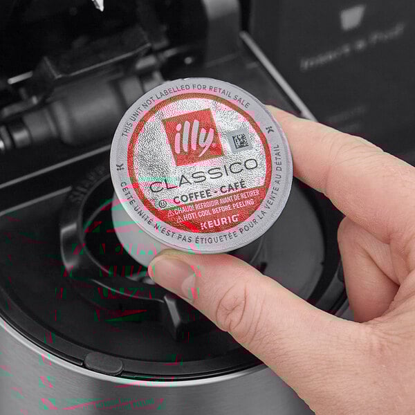 A hand holding a small round silver container with a red illy logo.