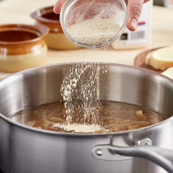 A person pouring McCormick Culinary Onion Powder into a pot of soup.