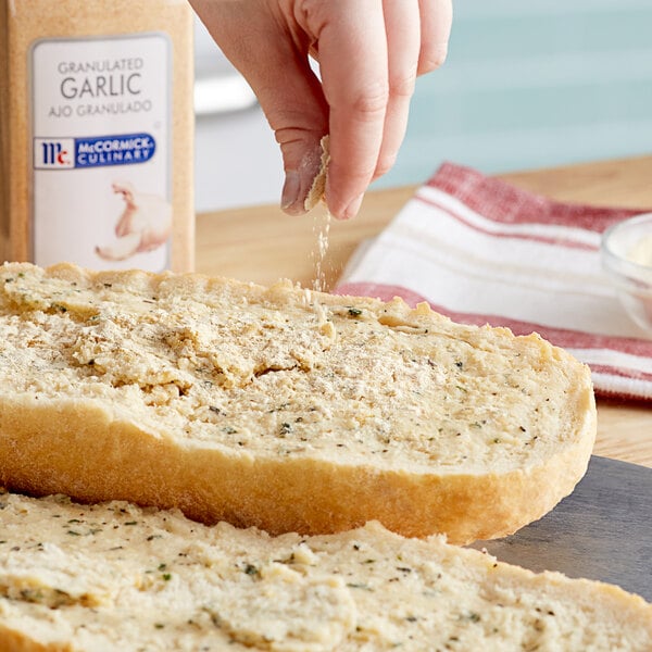 A hand sprinkling McCormick Culinary Granulated Garlic on a piece of bread.