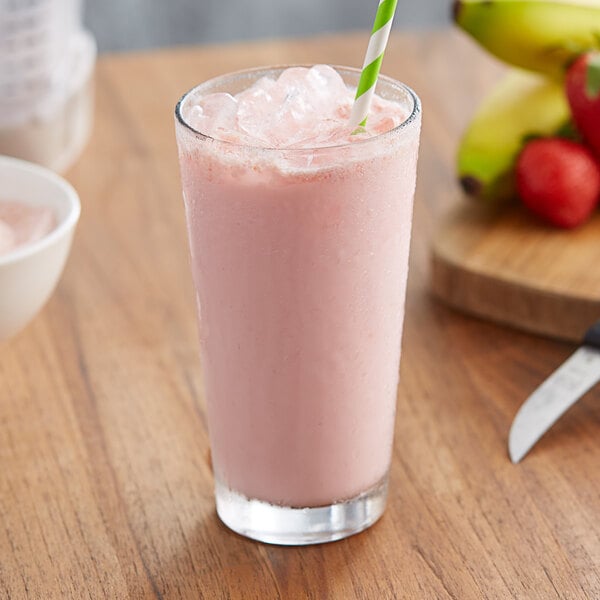 A glass of pink strawberry banana frappe with a straw.