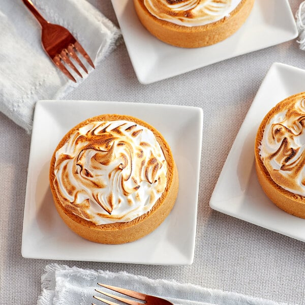 Three small pies with meringue on top of them, on a table in a bakery display.