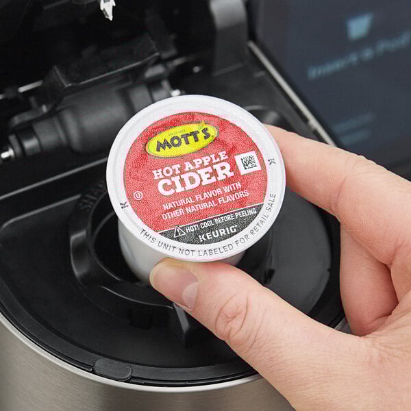 A hand holding a small container of Mott's hot apple cider.