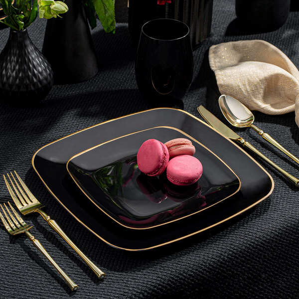 A black plastic coupe plate with a gold band on a table with pink and white cookies on it.