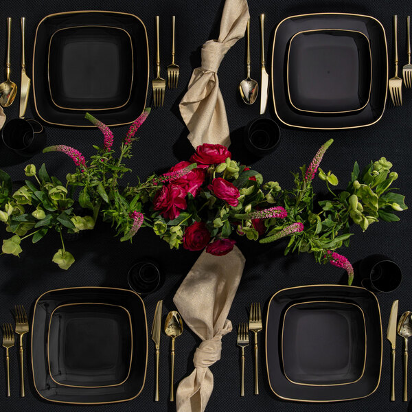 A table with black square plates with gold rims.