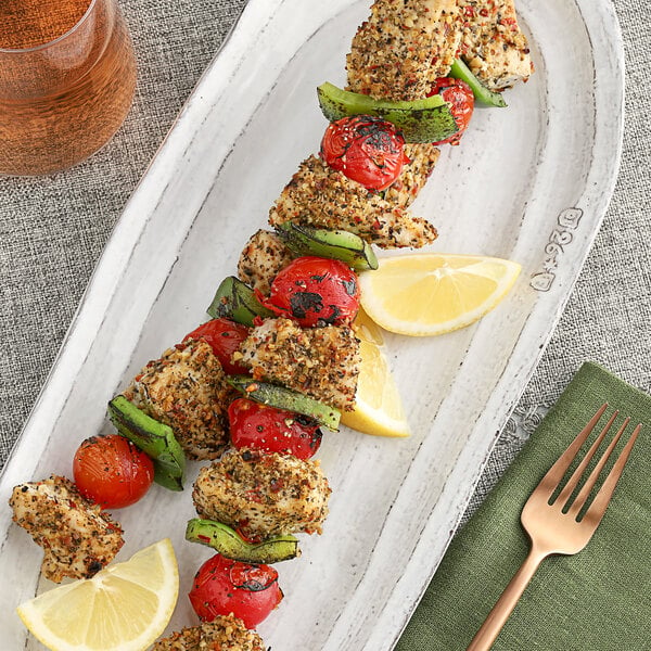 A plate with skewers of Mediterranean spiced chicken and vegetables with a lemon slice on the table.