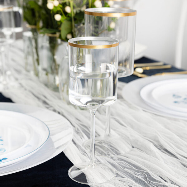 A table with Posh Setting clear plastic wine goblets with gold rims and plates.
