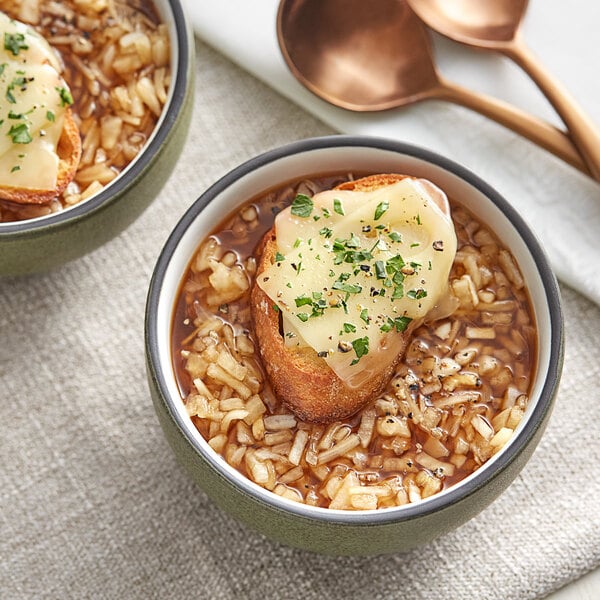 A close up of a bowl of soup with a piece of bread and cheese.