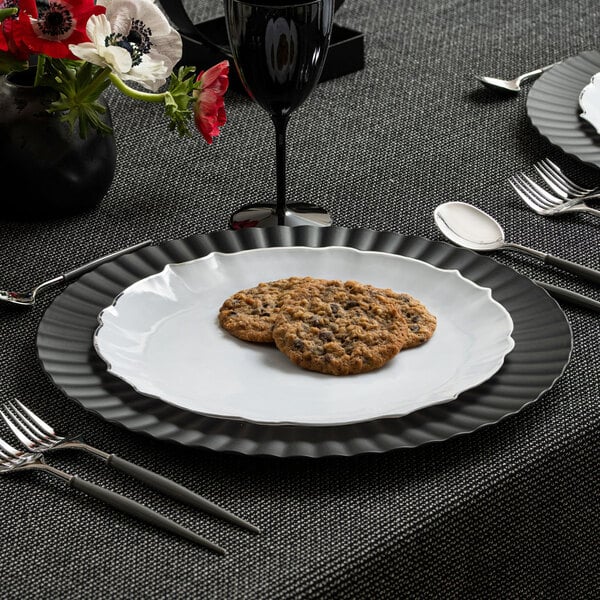 A Posh Setting white plastic plate with silverware and cookies on it.