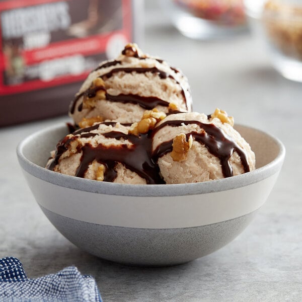 A bowl of ice cream with chocolate syrup drizzled on top and nuts.