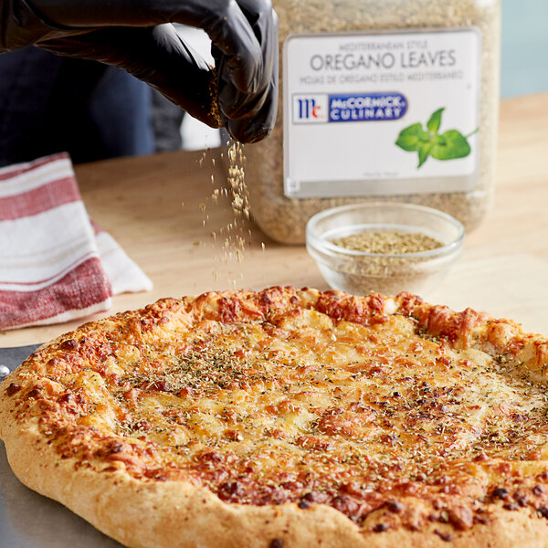 A person pouring McCormick Culinary Mediterranean Oregano onto a pizza.