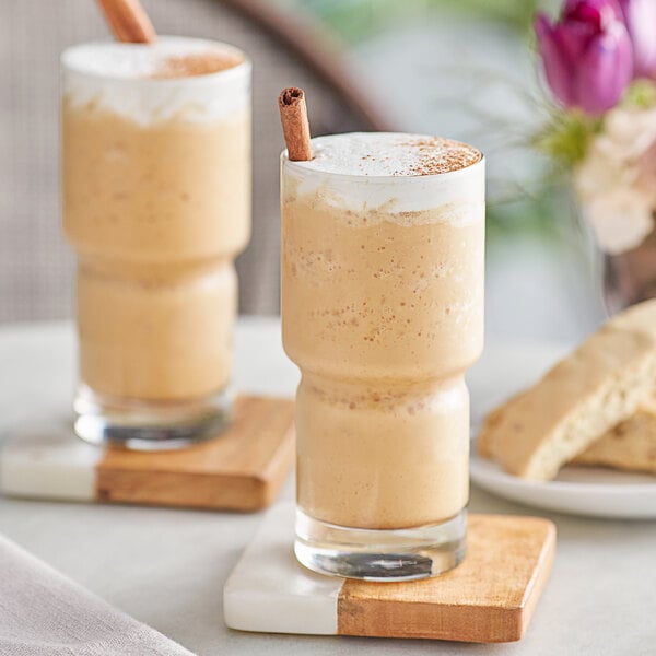 Two glasses of pumpkin spice blended ice coffee with cinnamon sticks on a table.