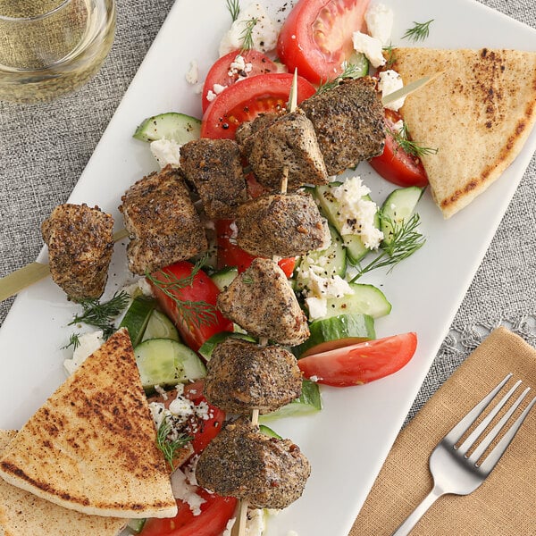 A plate of Greek food with meat on a skewer and a triangular piece of bread.