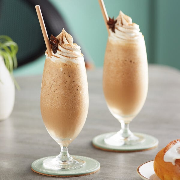 Two glasses of Big Train Pumpkin Pie Chai Tea Latte with whipped cream and cinnamon sticks.