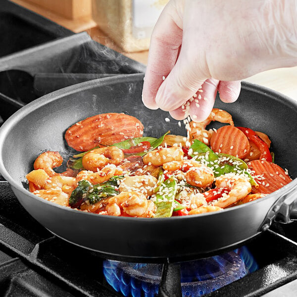 A hand sprinkling McCormick Culinary White Sesame Seeds over a pan of food.