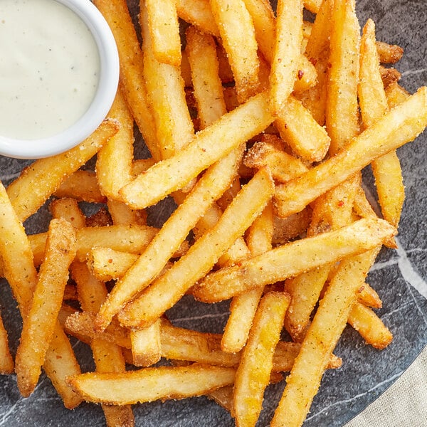 A plate of french fries with a small bowl of white sauce on the side.