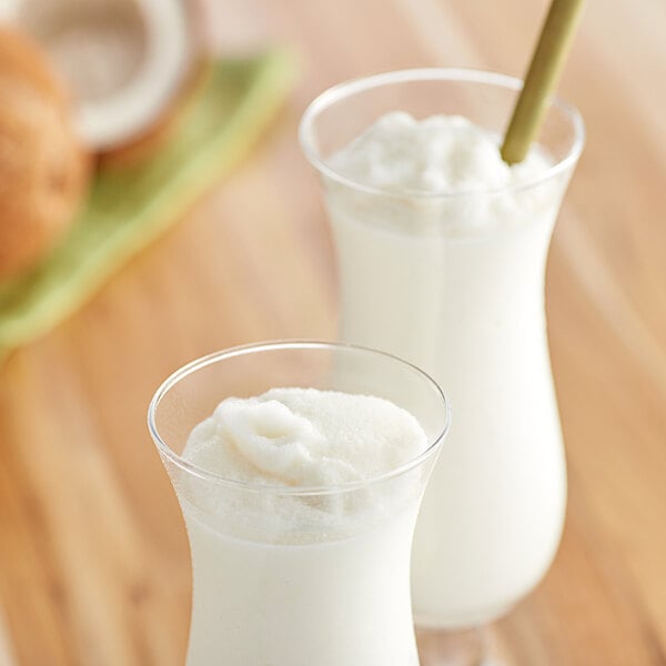 Two glasses of coconut milk with straws on a table.