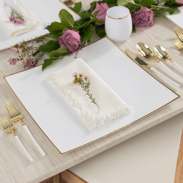 A white table set with a Posh Setting white charger plate with a gold rim and flowers on a table.