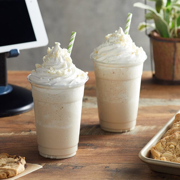 Two cups of Big Train white chocolate blended ice coffee on a table with cookies.