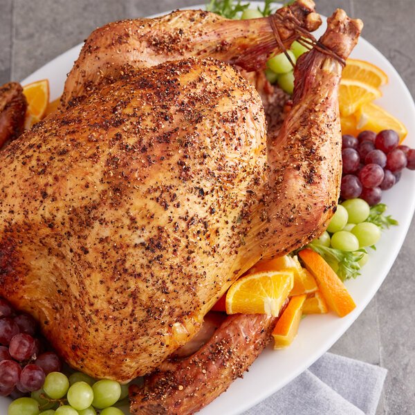 A whole roasted turkey on a plate with fruit including oranges and grapes.