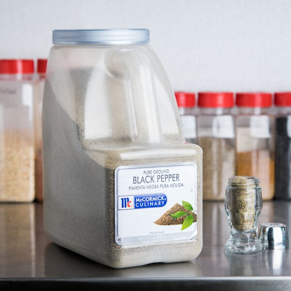 A plastic container of McCormick Culinary Ground Black Pepper next to other spices.