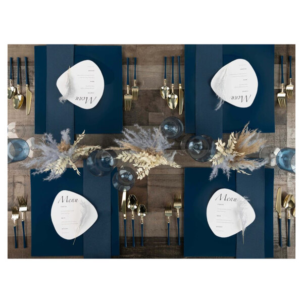 A table set with navy Posh Setting charger plates, gold cutlery, and blue and gold place settings.