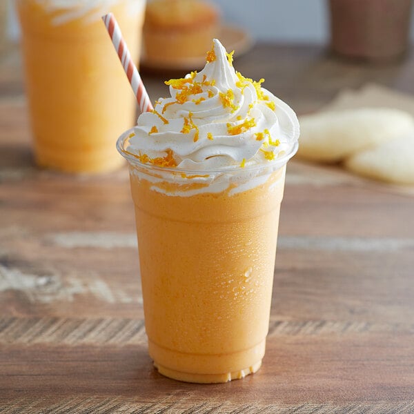 A glass of orange Big Train Kidz Kreamz Frappe with whipped cream and a straw.