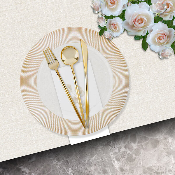 A white charger plate with a gold rope wide rim on a white table with gold silverware.