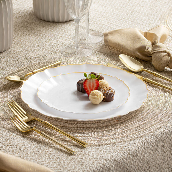 A white Posh Setting plastic plate with gold trim on a table with chocolates and strawberries.