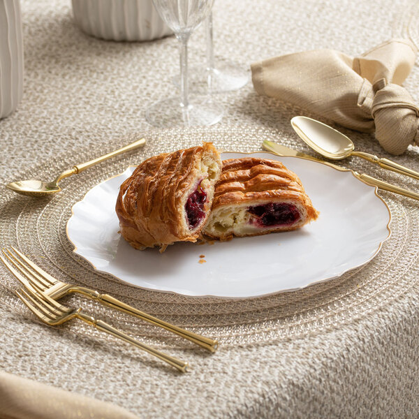 A Posh Setting plastic plate with a pastry and gold forks on it.