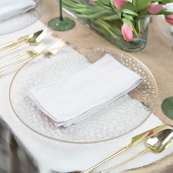 A table setting with a Posh Setting clear plastic charger plate with a gold rim, white plates, and gold forks.