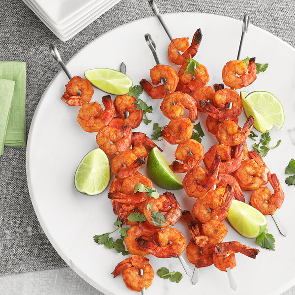 A plate of shrimp skewers with lime wedges next to a bowl of McCormick Culinary Mesquite Barbecue Seasoning.