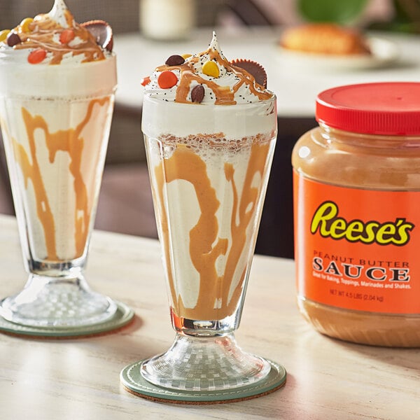 Two glasses of ice cream with peanut butter sauce and chocolate toppings on a table.