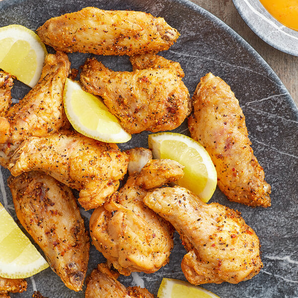 A plate of chicken wings with a lemon wedge on the side.