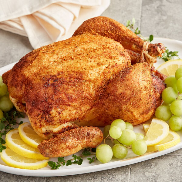 A plate of rotisserie chicken with lemon wedges and grapes.