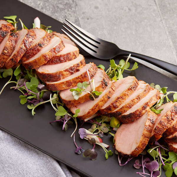 A plate of sliced meat with greens and a fork and knife.