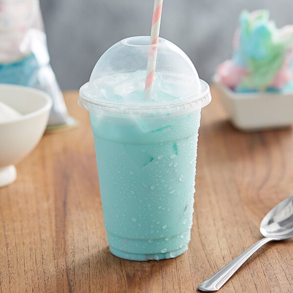 A blue drink in a plastic cup with a straw and a spoon on a table.